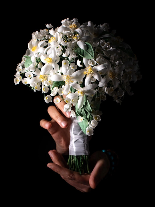 Primo piano di un bouquet alternativo bianco realizzato a mano da Jessica Ciaffarini, sorretto da due mani su sfondo nero.