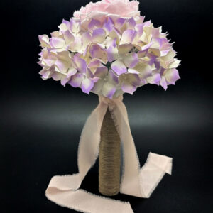 Profilo intero di un bouquet di carta con ortensie viola, impugnatura rivestita in corda naturale e un lungo fiocco in chiffon rosa antico.